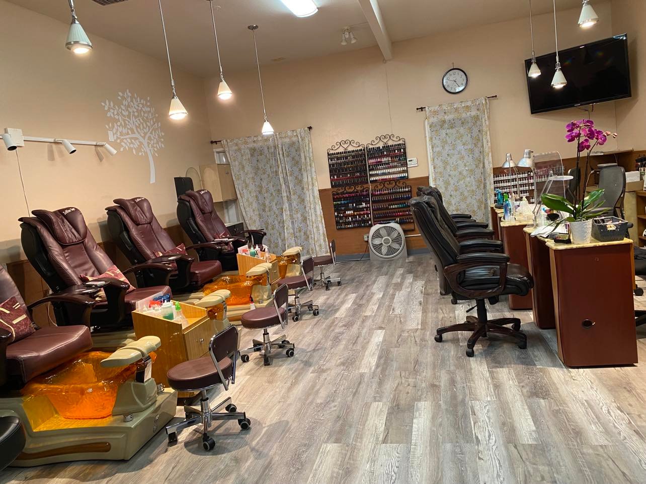 Inside Unique Nails: burgundy pedicure chairs, manicure tables, a polish wall, and an orchid.
