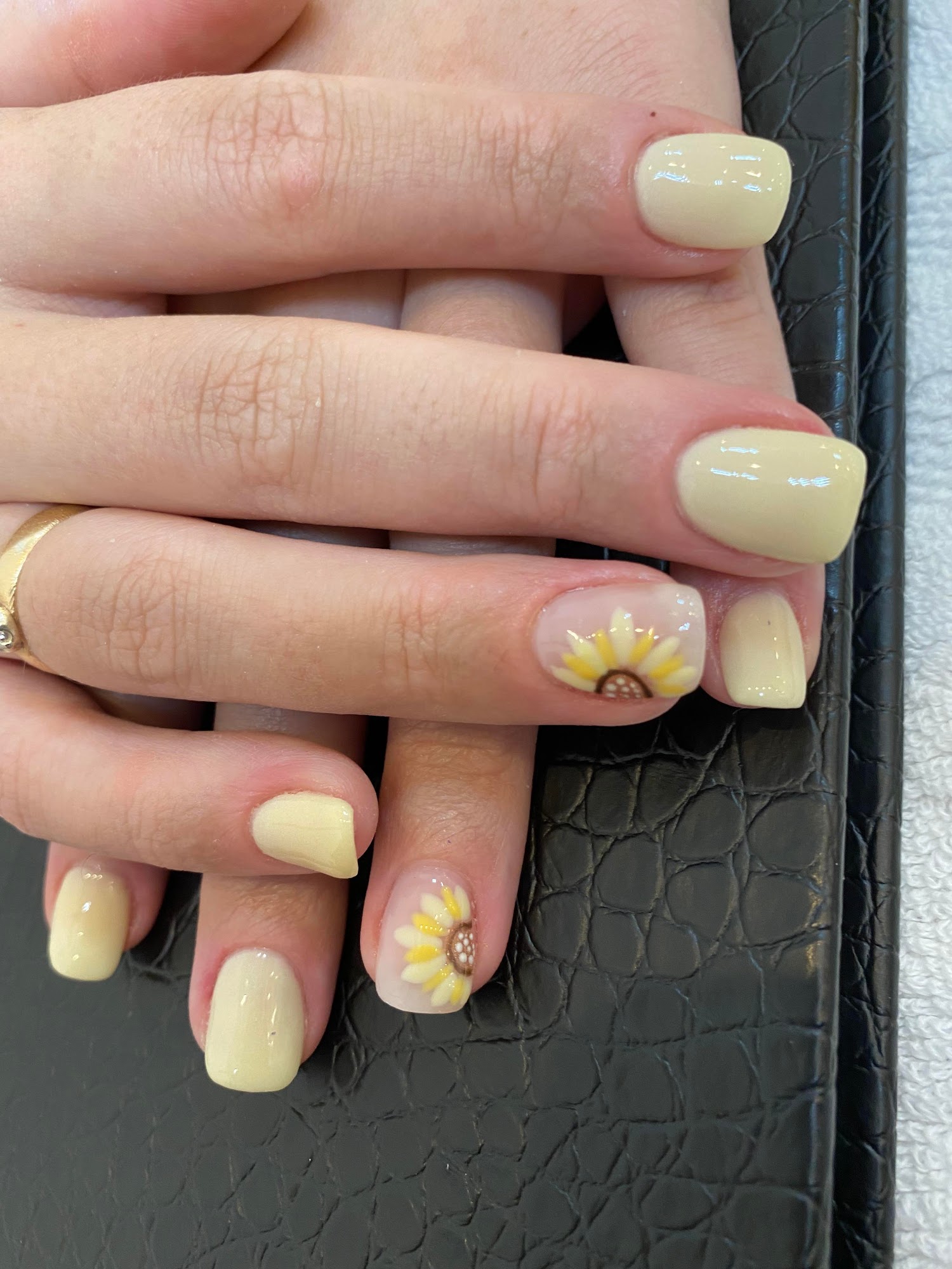 Short cream manicure with two sunflower nail-art accents.